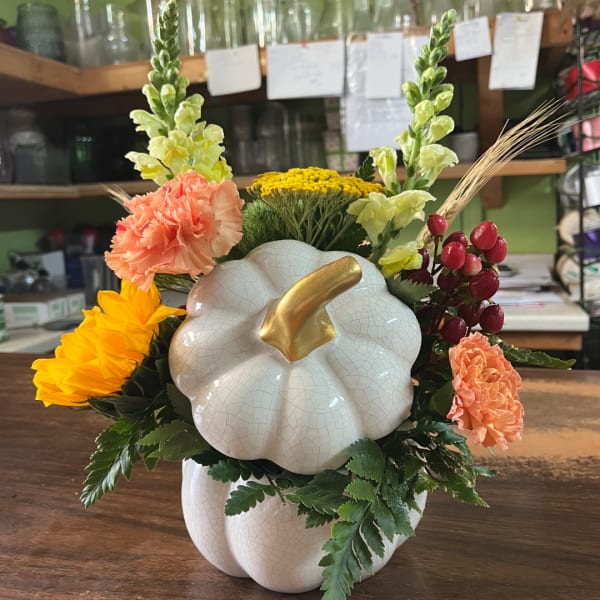 Pumpkin-shaped floral arrangement with yellow and peach flowers in a white vase
