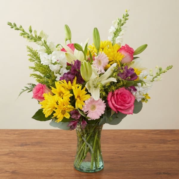 Mixed bouquet of pink, yellow, white, and purple flowers in a glass vase