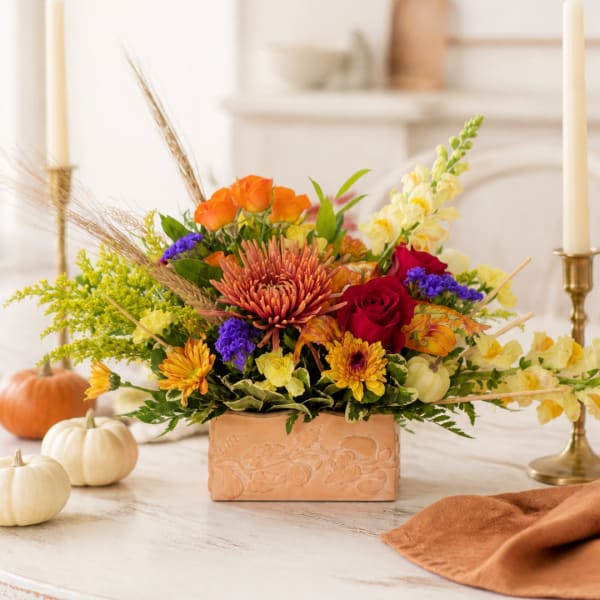 Autumn floral arrangement in a peach rectangular vase with pumpkins nearby