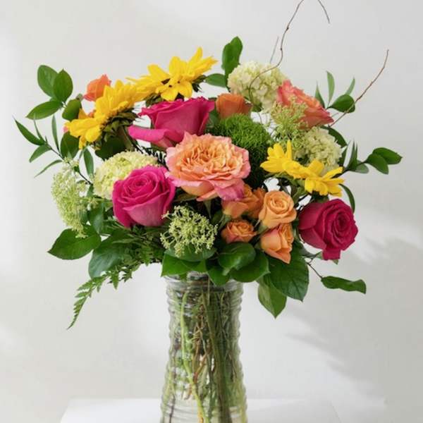 Mixed bouquet of pink, peach, and yellow flowers in a clear glass vase