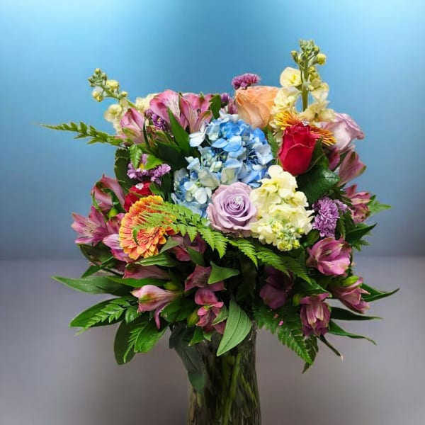 Mixed bouquet in a clear glass vase with blue hydrangea and pink, purple, and yellow flowers
