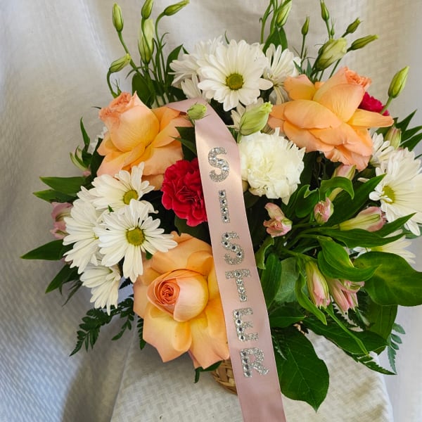 Peach roses and white daisies in a basket with a pink ribbon