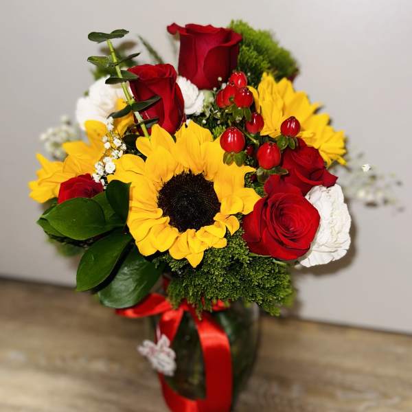 Bouquet of red roses and yellow sunflowers in a glass vase with a red ribbon.