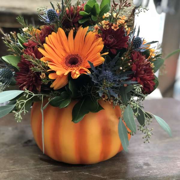 Orange and burgundy floral arrangement in a pumpkin-shaped container