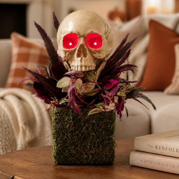 Skull decoration with glowing red eyes and purple foliage in a moss-covered container