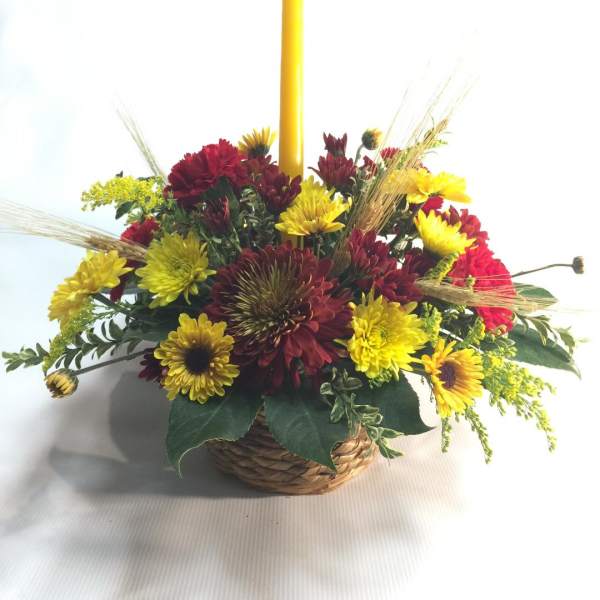 Basket arrangement of yellow and red flowers with a tall yellow candle