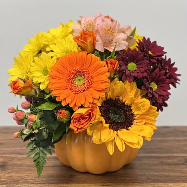 Mixed bouquet in a pumpkin-shaped container with yellow, orange, pink, and burgundy flowers