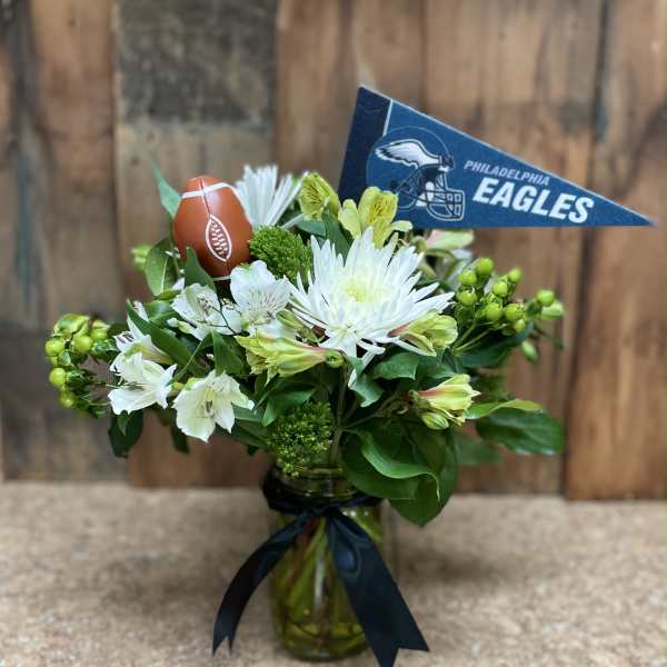 White flowers in a glass vase with a Philadelphia Eagles pennant and football decoration