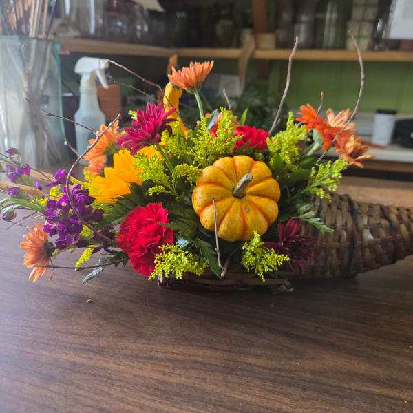 Autumn floral arrangement with a small pumpkin centerpiece in a basket