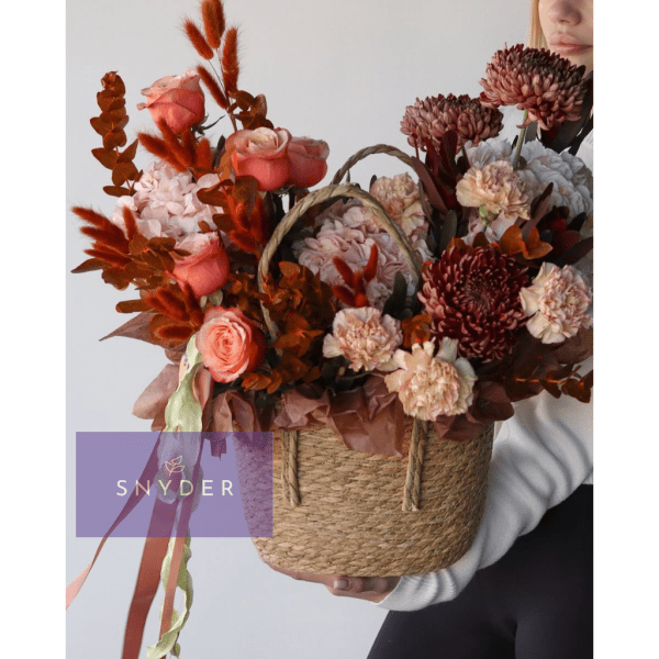 Basket of coral and cream flowers with ribbons, held by a person
