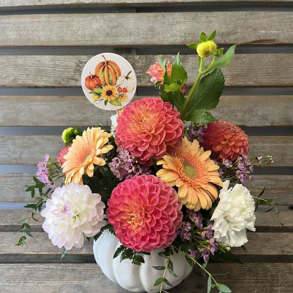 Fall floral arrangement in a white pumpkin container with colorful blooms and a pumpkin pick