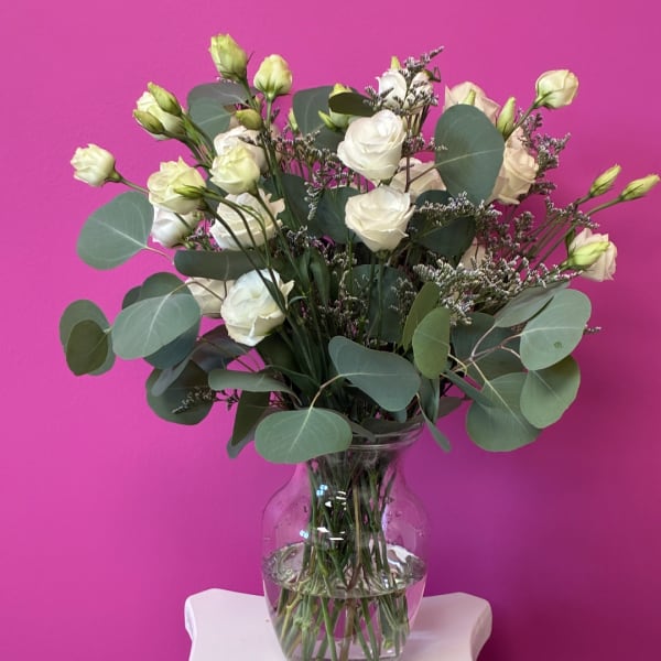 White roses and buds in a clear glass vase with round eucalyptus leaves