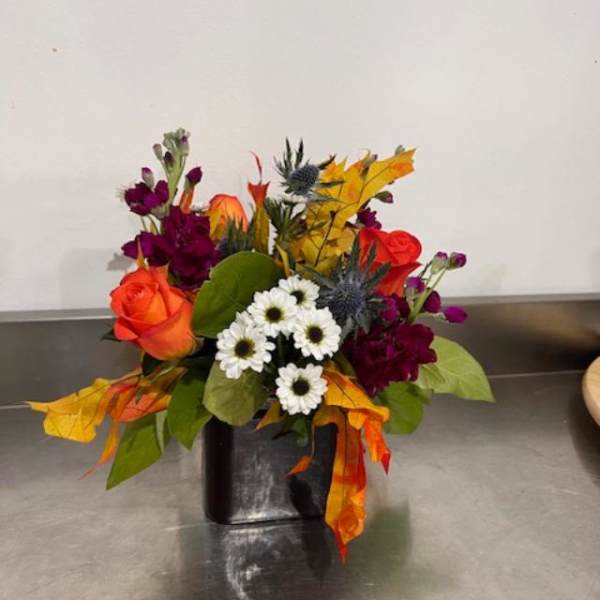 Mixed bouquet with orange roses, white daisies, and purple flowers in a black vase