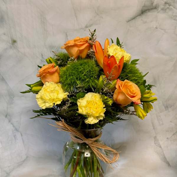 Orange roses and yellow carnations in a glass vase with raffia tie