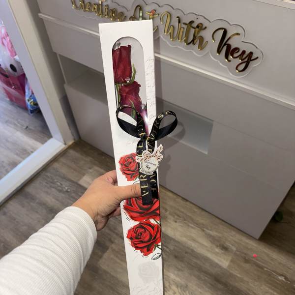 Two red roses in a tall white gift box with a black ribbon