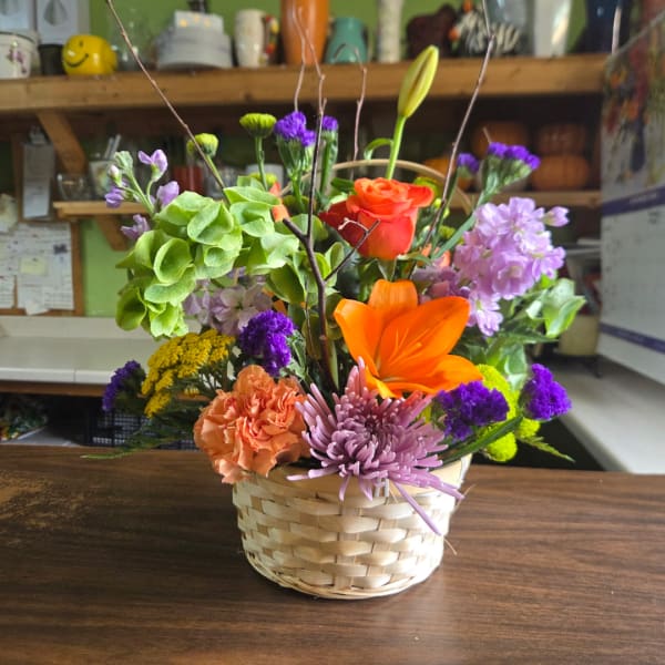 Mixed flower arrangement in a woven basket with orange and purple blooms
