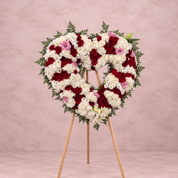Heart-shaped floral wreath on a wooden easel with red, white, and pink flowers