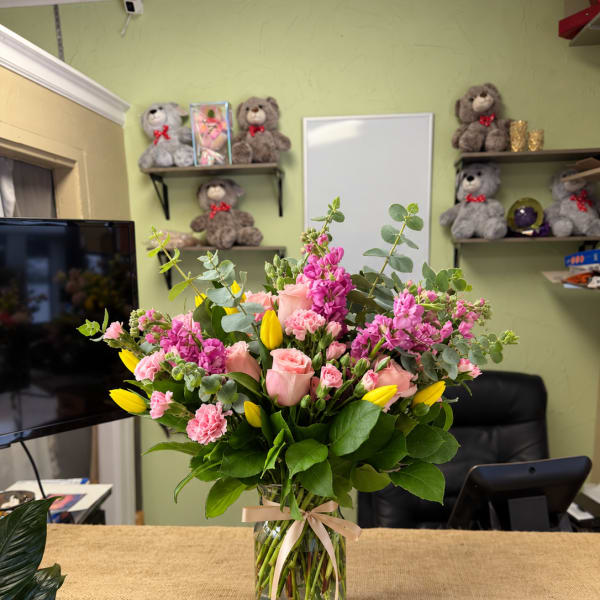 Pink and yellow flower arrangement in a glass vase with ribbon