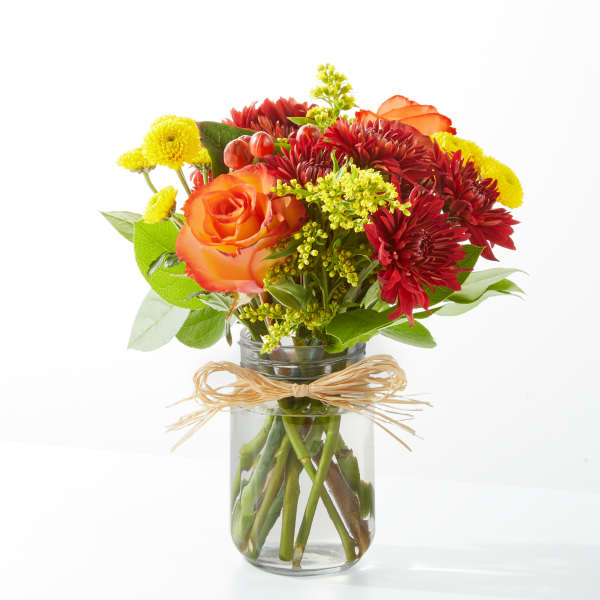 Bouquet of orange roses, red chrysanthemums, and yellow mums in a glass jar vase