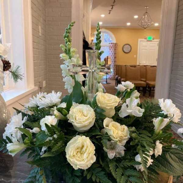 White floral arrangement with roses and lilies around a glass cross