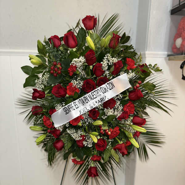Standing floral spray of red roses and lilies with a white ribbon on an easel