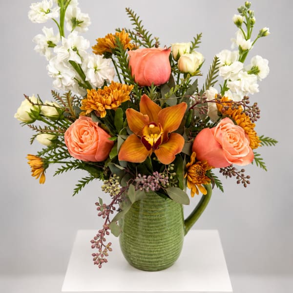 Peach roses and orange blooms in a green ceramic pitcher