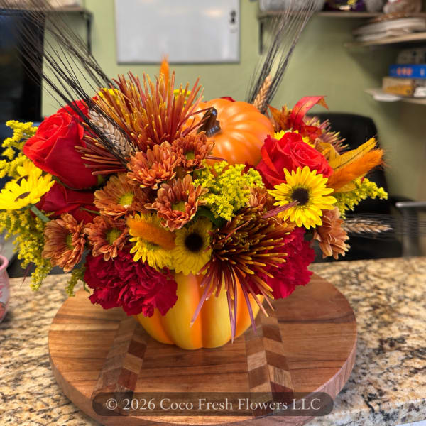 Autumn floral arrangement in a pumpkin-shaped container with red and yellow blooms