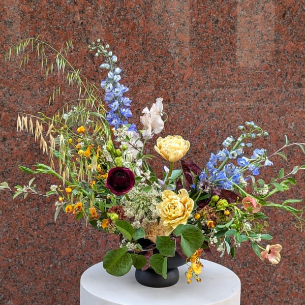 Mixed floral arrangement in a black vase with blue, yellow, and burgundy blooms