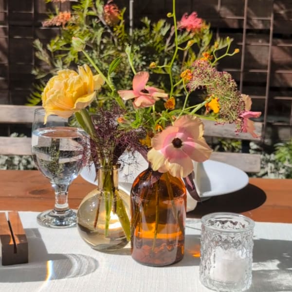 Two small floral arrangements in glass vases on a table with candles and glassware.