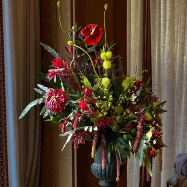 Tall floral arrangement with red anthuriums and yellow accents in a dark vase