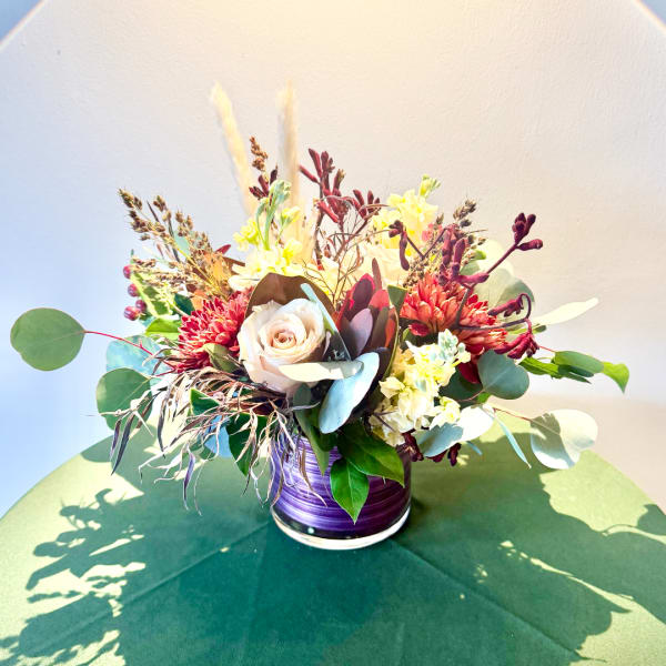 Mixed floral arrangement in a purple vase with cream and red blooms