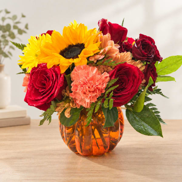 Bouquet of red roses, sunflowers, and carnations in an orange glass vase