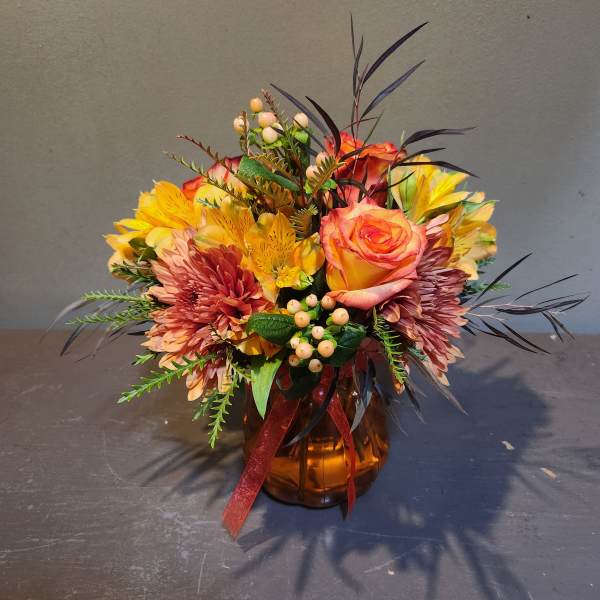 Mixed bouquet of orange, yellow, and pink flowers in an amber vase