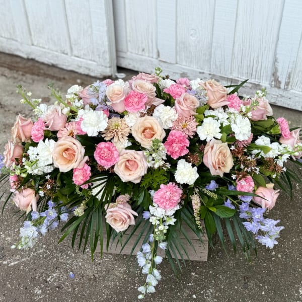 Large pastel floral arrangement with roses, carnations, and blue flowers in a wooden box