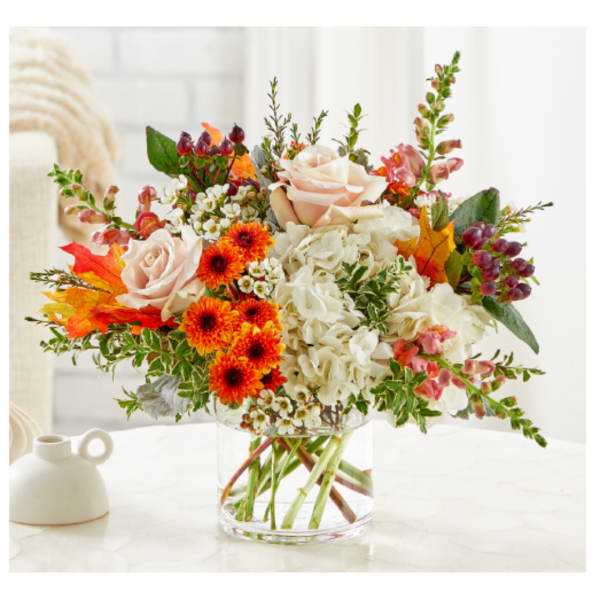 Mixed bouquet of roses, hydrangeas, and orange blooms in a clear glass vase