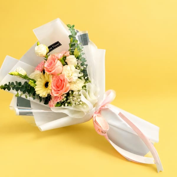 Bouquet of pink and white flowers wrapped in white paper with a ribbon