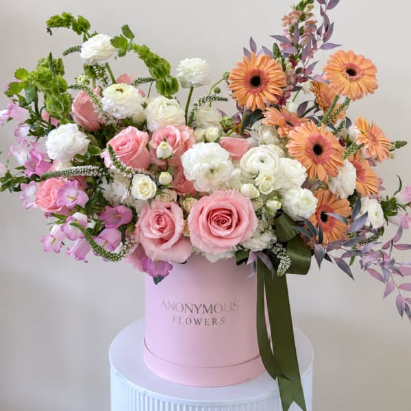 Pink and white mixed bouquet in a pink hatbox with orange daisies