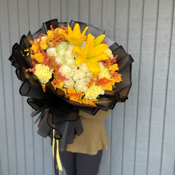Yellow lilies and white roses in a black-wrapped bouquet