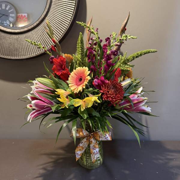 Colorful mixed flower arrangement in a glass vase with a patterned ribbon