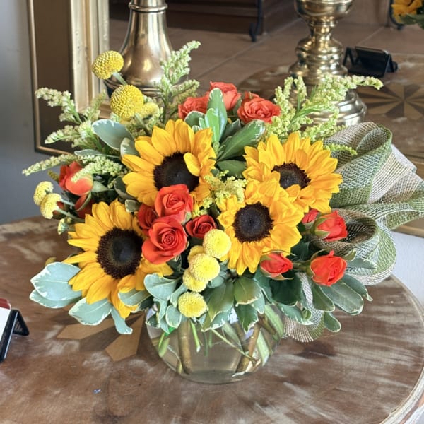 Sunflower and orange rose bouquet in a glass vase with a burlap bow