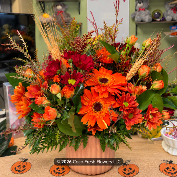 Orange and red mixed flower arrangement in a peach vase