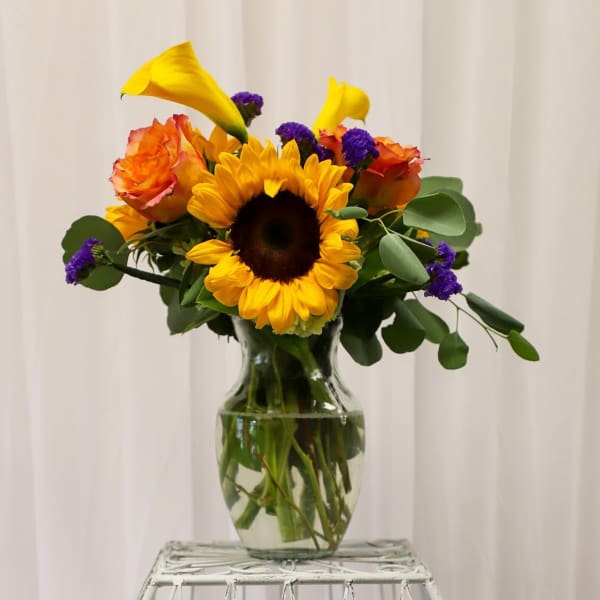 Sunflower bouquet with orange roses and purple accents in a glass vase