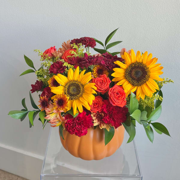 Sunflowers and mixed blooms arranged in a pumpkin-shaped container