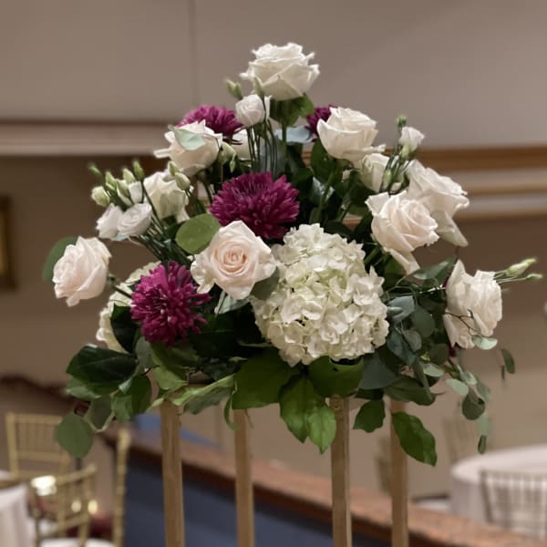 White roses and purple mums arranged in a tall centerpiece