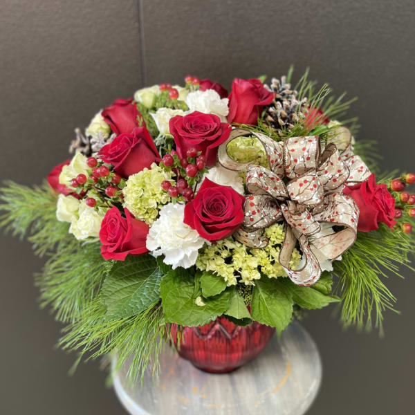 Red roses and white flowers arranged in a red vase with a decorative ribbon