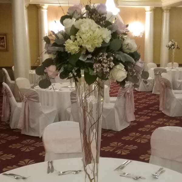 Tall white floral centerpiece in a clear glass vase on a banquet table