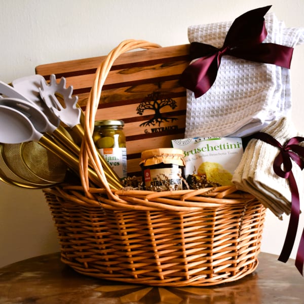 Gift basket with kitchen towels, utensils, and food items in a wicker basket
