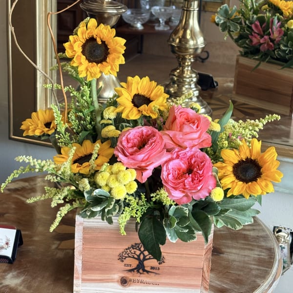 Pink roses and sunflowers arranged in a wooden box