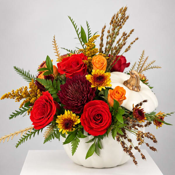 Autumn floral arrangement in a white pumpkin container with red and orange blooms