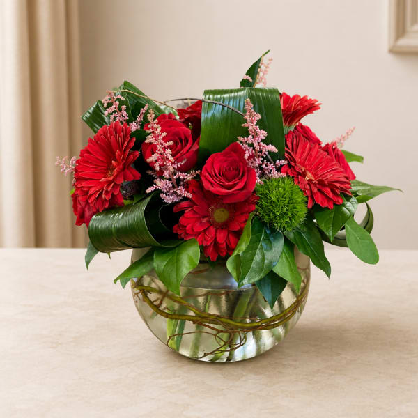 Red roses and gerbera daisies in a glass bowl vase